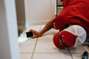 man on the ground using his phone flashlight to look under a door